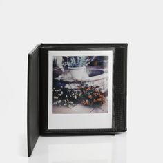 an old photo frame with flowers in it on a white table next to a potted plant