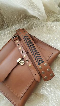 a brown leather wallet sitting on top of a white cloth covered bed with an arrow design