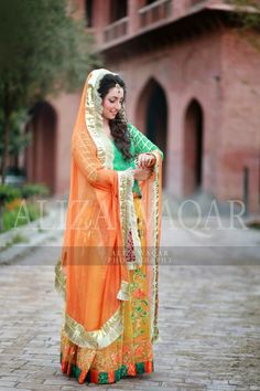 a woman in an orange and green outfit standing on a brick walkway with her arms around her waist