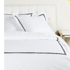 a bed with white sheets and black piping on the headboard, next to a night stand