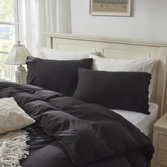 a bed with black sheets and pillows on top of it next to a night stand