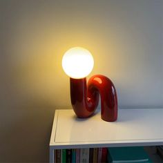 a red lamp sitting on top of a white table next to a bookshelf