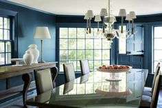 a dining room with blue walls and white chandelier hanging from the ceiling above a glass table surrounded by chairs