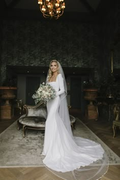 a woman in a white wedding dress holding a bouquet and posing for the camera with a chandelier above her