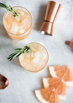 two cocktails with rosemary garnish sit on a marble table next to copper shakers