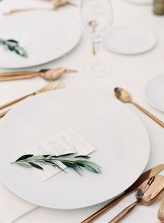 the table is set with white plates and gold utensils