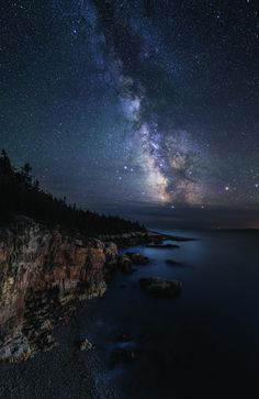 the night sky is filled with stars and clouds above some rocky coastlines, as well as