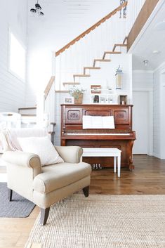 a living room filled with furniture and a grand piano in front of a stair case