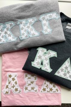 three t - shirts with letters and stars on them sitting on a table next to each other