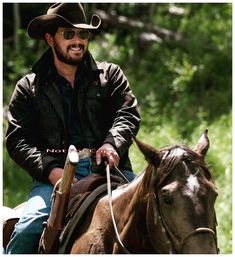 a man riding on the back of a brown horse next to a lush green forest