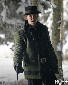 a man with a hat and coat walking in the snow