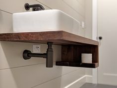 a white sink sitting on top of a wooden shelf next to a wall mounted faucet