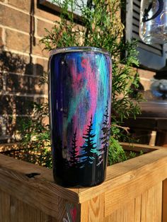 a colorful vase sitting on top of a wooden table next to a planter filled with flowers