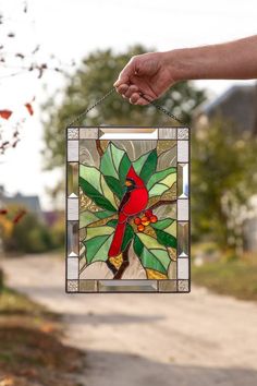 a hand holding a stained glass window with a cardinal on it's back and green leaves