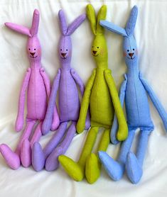 four different colored stuffed animals sitting next to each other on a white sheet in the shape of bunnies