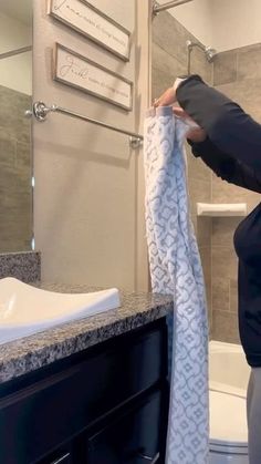 a woman holding up a towel in front of a bathroom sink