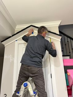 a man on a ladder painting the trim of a house's door with paint rollers