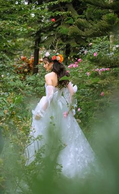 a woman in a white dress is walking through the woods with flowers on her head