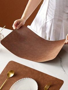 a woman is cutting paper on top of a place mat with goldware in front of her