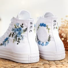 a pair of white shoes with blue flowers painted on them sitting on top of a table