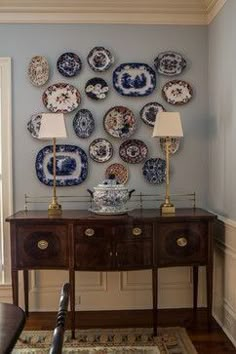 a dining room table with plates on the wall above it and a lamp next to it