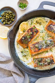 some fish is cooking in a skillet with lemons and olives on the side