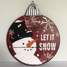 a wooden sign that says let it snow with a snowman on it's face