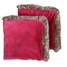 two pink velvet pillows with fringes on the edges and one has a white background