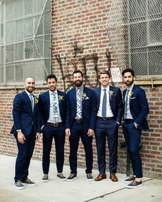 a group of men standing next to each other in front of a wall with graffiti on it