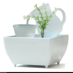 there is a white vase with two cups and a green plant in the cup holder