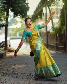 a woman in a yellow and blue sari dancing on the street with her arms outstretched