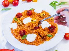 a person holding a fork over a plate of pasta with tomatoes and mozzarella