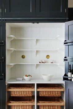 a kitchen with black cabinets and white counter tops, baskets on the bottom shelf in front of the open door