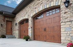 two large brown garage doors in front of a brick building with flowers on the sidewalk