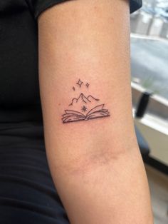 a woman's arm with a book and stars tattoo on the left side of her arm