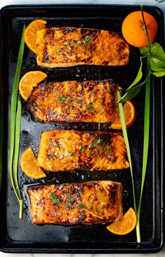 grilled salmon with oranges and green onions on a black tray next to an orange