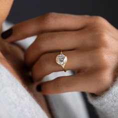 a woman's hand wearing a gold ring with a white diamond on the side