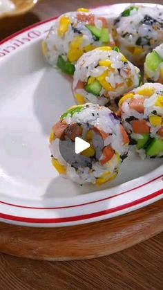 sushi rolls on a white plate with red and white trim around the edges, sitting on a wooden table