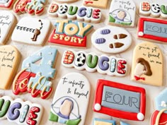 many decorated cookies are displayed on a white tablecloth with writing and pictures in different colors