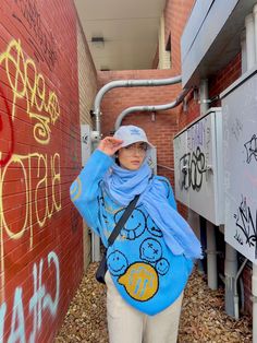 a woman is standing in front of a brick wall with graffiti on it and wearing a blue scarf around her neck