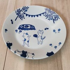 a blue and white plate with cats on it sitting on a wooden table next to a wall