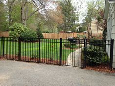 a black iron fence in front of a house with trees and bushes around the yard