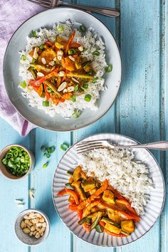 two plates filled with rice and vegetables on top of a blue wooden table next to silverware