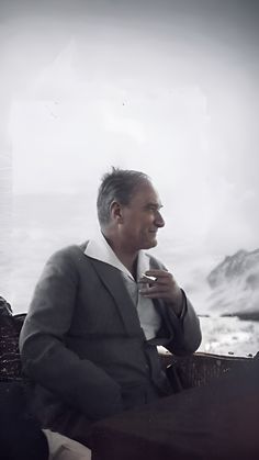 a man sitting on top of a wooden bench holding a cup in his hand and looking off into the distance