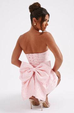 THE dress of the season has landed and you're going to be obsessed. Meet Elenora, our dreamy mini with a pretty structured skirt and waist cinching bodice. This strapless style is complete with lace up and an oversized bow to the back for perfect feminine drama.     Colour: Blush.  Premium non-stretch floral jacquard.  Strapless design.  Waist cinching.  Detachable bow.  Oversized bow detail to back.  Voluminous, structured skirt.  Lace up to the reverse.  Mini length.  Model is an XS and is wea Grad Party Dresses, Couqutte Outfit, Formal Dresses Mini, Winter Formal Dresses Short, Homecoming Dresses Corset, Structured Skirt, Hoco Inspo, Mini Dress With Bow, Midi Dress Wedding Guest