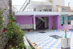 a purple and white building with stairs leading up to the second floor, surrounded by greenery