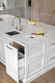 a kitchen with white cabinets and marble counter tops, an island sink and dishwasher