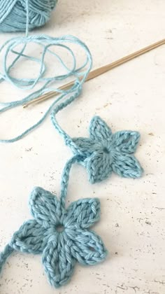 two crocheted flowers sitting on top of a table next to yarn