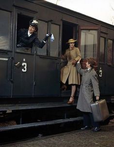 three people are standing on the side of a train car and one person is holding a suitcase