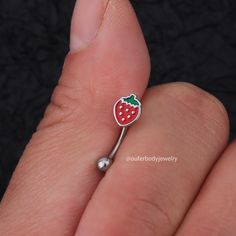 a person's hand holding a tiny strawberry shaped nose ring with a green leaf on it